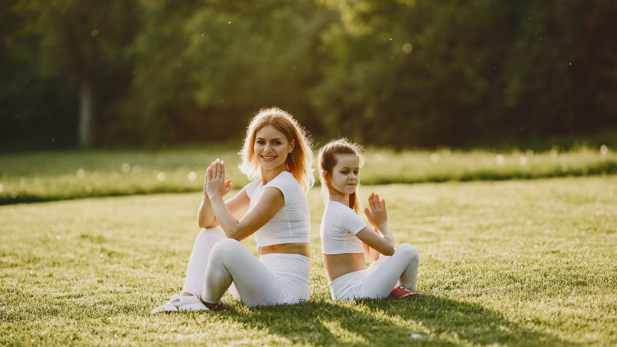 Mother and daughter practicing yoga in matching outfits on grass outdoors, enjoying a sunny day.